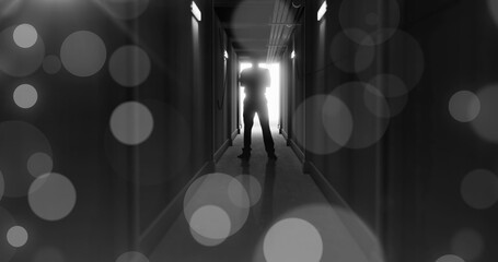 Obraz premium Image of grey bokeh light spots over scary figure backlit in doorway at end of dark corridor