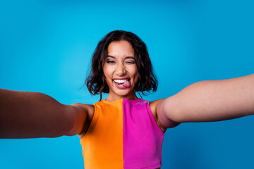 Happy young woman in stylish colorful attire taking a selfie against a vibrant blue background
