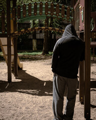 A strange suspicious man in a hood stands on the playground