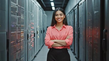 Confident server room technician standing with a smile in a high-tech server room. She has arms crossed, looks proud and capable