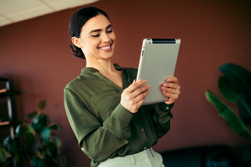 Smiling businesswoman using a digital tablet in a modern office setting with stylish decor and a...