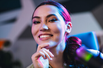 Professional young woman working with a microphone, sitting indoors, illuminated by colorful...