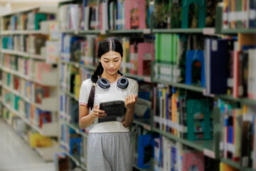 A female student is browsing books on a shelf in the library, focused on finding the right material for her studies.