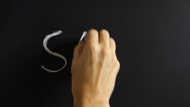 Closeup view of hand writing SALE on black chalkboard background. Concept of promotion announcement, advertising, discount, tax cut, tariffs increase, off season price decrease, special rate offer