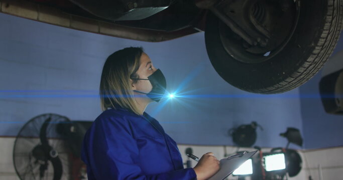 Image of light spots over woman with face mask repairing car