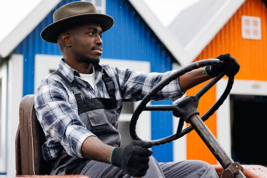 Confident African American Farmer man operating Tractor on Rainy Day in Colorful Farm Setting. Agriculture and Farm Life Concept. - Powered by Adobe