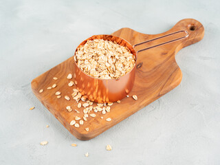 Rolled oats in measuring cup on wooden board