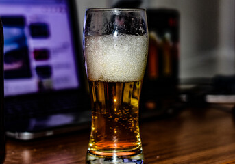 A beer glass with foam and condensation on a wooden table.