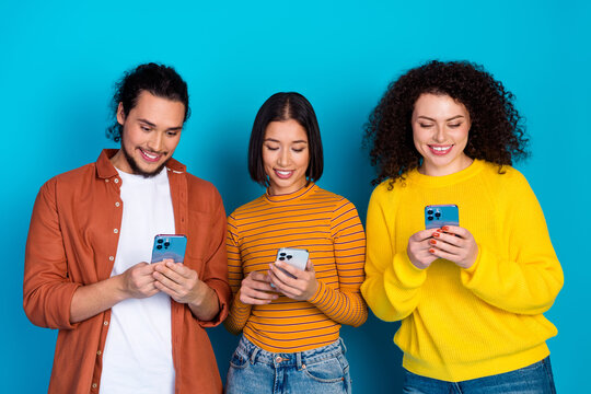 Young friends sharing mobile devices and laughter on a vibrant blue background, showcasing friendship and technology