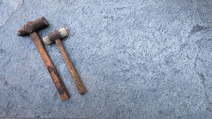 Metal and rubber hammer lying on grey textured stone surface, leaving ample copy space for text or design elements. Copy space