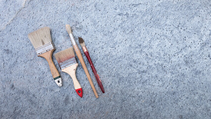 Painting brushes scattered across gray textured backdrop, preparing for creative art session. Copy space