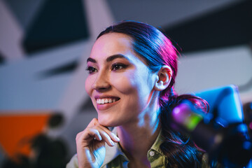 Smiling woman with vibrant lighting speaks into a microphone during a live broadcast or interview...