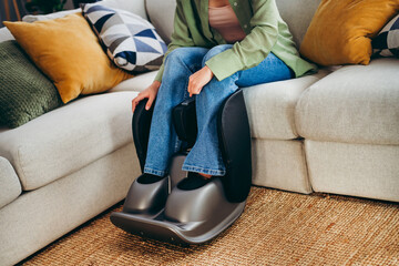 Young woman enjoying a relaxing foot massage at home in a cozy living room with a modern massager