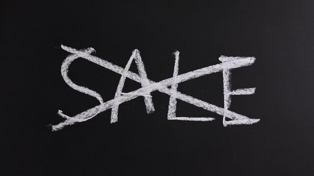 Closeup view of hand crosses out SALE on black chalkboard background. End of discount, special rate offer, promotion announcement, advertising, tax cut, tariffs increase, off season price decrease