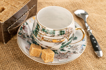 One ceramic cup with sugar on a saucer on a jute cloth, close-up