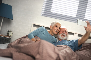 Senior couple taking a selfie in the bed