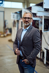 Fototapeta premium Confident Businessman Standing in Modern Industrial Workspace Holding Clipboard