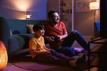 Happy father and his son playing video games on floor in living room at night