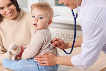 Pediatrician examining baby with stethoscope in clinic, closeup