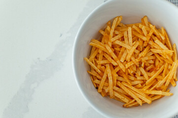 Overhead View of Fried Potato Chips in a White Bowl on Kitchen Counter. Golden Crispy Potato Chips Served in a White Bowl on a Clean Countertop. Top-Down Shot of Freshly Fried Potato.