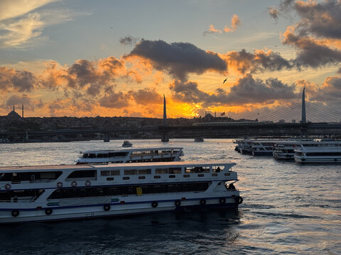 Passenger ferry crossing golden horn at sunset with dramatic clouds and halic metro bridge
