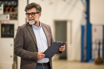 Professional Man Smiling While Holding a Clipboard in an Industrial Workplace