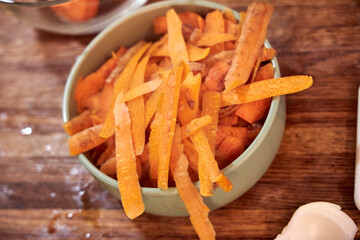 A simple bowl filled with fresh carrot peels sits on a rustic wooden countertop in the kitchen. The image reflects everyday cooking moments, food preparation, and the natural textures of vegetables an