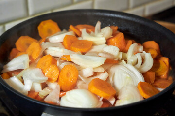 Sliced carrots and onions sizzling in a frying pan on a stove. The image captures the process of cooking a homemade meal, with vibrant colors, steam, and warm lighting emphasizing the freshness 