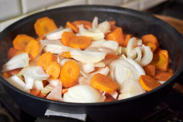 Sliced carrots and onions sizzling in a frying pan on a stove. The image captures the process of cooking a homemade meal, with vibrant colors, steam, and warm lighting emphasizing the freshness 