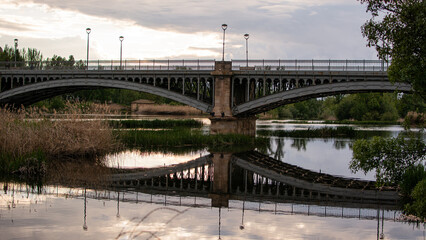 Iron bridge with reflection on calm river at sunset in urban park