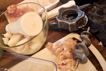 A woman carefully cleaning raw meat remnants from a meat grinder blade in a kitchen. The image reflects food preparation, hygiene, and the process of making homemade ground meat