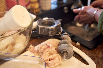 Fototapeta premium A woman carefully cleaning raw meat remnants from a meat grinder blade in a kitchen. The image reflects food preparation, hygiene, and the process of making homemade ground meat