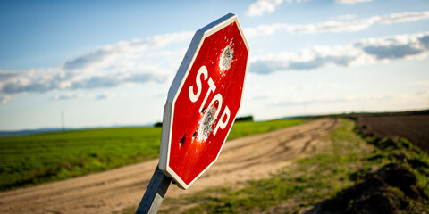 Damaged stop sign with bullet holes on rural dirt road