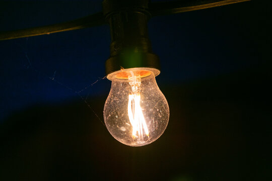 Light bulb is lit up in the dark. The light is warm and inviting. The bulb is glowing with a soft, yellow light.