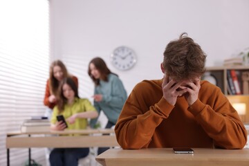 Teenage boy with smartphone suffering from bullying at school, selective focus