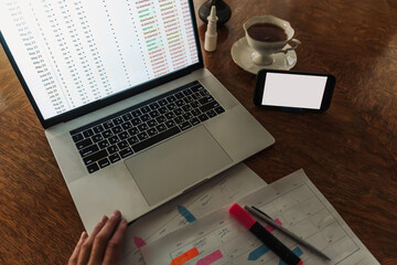 Blank smartphone screen on a home office desk with laptop and printed planning sheets. Modern remote work lifestyle and analytics concept