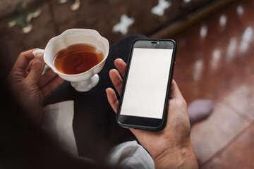 Smartphone with blank screen held by woman on balcony, suitable for app design mockups or digital lifestyle visuals. Peaceful outdoor moment