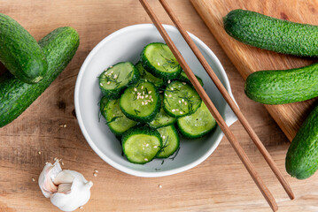 Sunomono, japanese cucumber salad. Sliced cucumbers with asian dressing of soy sauce, rice vinegar, sesame oil, sugar nd dill in white bowl on wood table. 