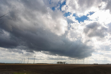 Dramatic cloud formation over a flat landscape with wind turbines in the distance on a cloudy day