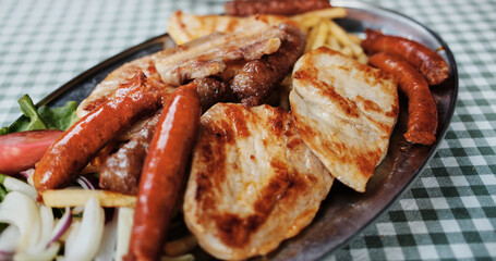 Close-up of a traditional Serbian grilled meat platter with sausages, pork and French fries served on a metal plate. Balkan cuisine.