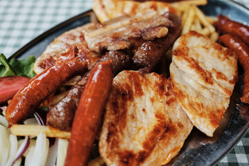 Close-up of a traditional Serbian grilled meat platter with sausages, pork and French fries served on a metal plate. Balkan cuisine.
