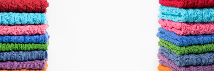 Set of multicolored knitted clothes stacked on a gray background with space for text. Knitting warm clothes, blankets and blankets. Concept of home needlework. Banner