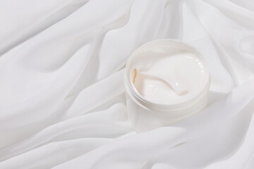 Minimalist skincare scene featuring a white whitening cream container elegantly placed on soft white satin, symbolizing purity and luxury.