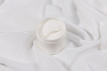 Minimalist skincare scene featuring a white whitening cream container elegantly placed on soft white satin, symbolizing purity and luxury.