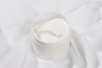 Minimalist skincare scene featuring a white whitening cream container elegantly placed on soft white satin, symbolizing purity and luxury.