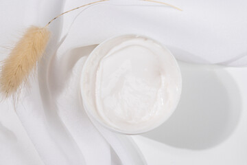 Minimalist skincare scene featuring a white whitening cream container elegantly placed on soft white satin, symbolizing purity and luxury.