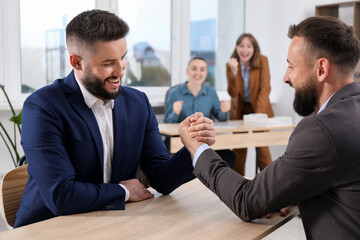 Businessmen arm wrestling at wooden table in office, selective focus