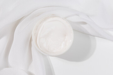 Minimalist skincare scene featuring a white whitening cream container elegantly placed on soft white satin, symbolizing purity and luxury.