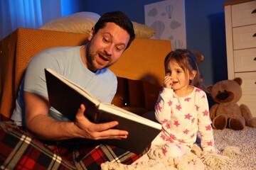 Emotional father reading bedtime story to his daughter on floor at home