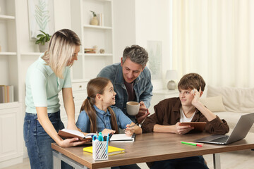 Happy parents and their children doing homework with laptop at table indoors